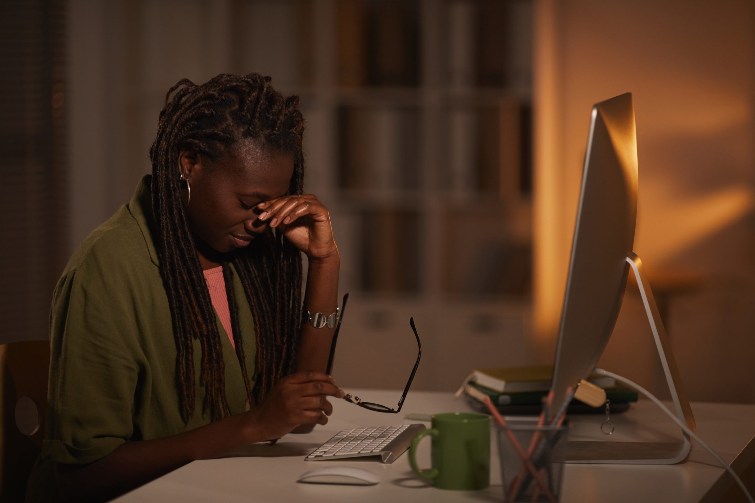 Side view portrait of exhausted African-American woman rubbing eyes while working late at night in dark office, copy space